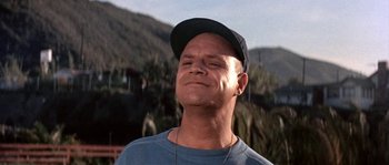 Movie still from “Muscle Beach Party” (1964), directed by William Asher – A man in a hat and a blue t - shirt is smiling; Close Up shot, Low angle