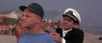 Movie still from “Muscle Beach Party” (1964), directed by William Asher – A man is shaving another man's beard while a crowd watches; Medium shot, Low angle