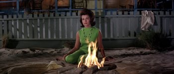 Movie still from “Muscle Beach Party” (1964), directed by William Asher – A woman sitting on the ground near a fire pit; Medium shot, High angle