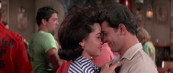 Movie still from “Muscle Beach Party” (1964), directed by William Asher – A man and a woman kissing each other in front of a crowd; Close Up shot, Over the shoulder angle