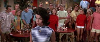 Movie still from “Muscle Beach Party” (1964), directed by William Asher – A group of people standing around a room with drinks on the tables; Medium shot, Low angle