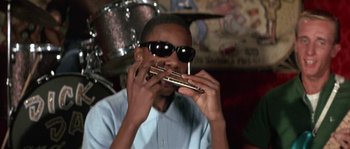 Movie still from “Muscle Beach Party” (1964), directed by William Asher – A man in sunglasses playing a musical instrument; Close Up shot, Low angle