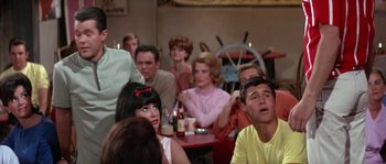 Movie still from “Muscle Beach Party” (1964), directed by William Asher – A group of people sitting around a table; Medium shot, Over the shoulder angle