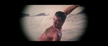 Movie still from “Muscle Beach Party” (1964), directed by William Asher – A man standing on a beach with his arms up; Medium shot, Low angle