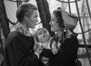 Movie still from “Mutiny on the Bounty” (1935), directed by Frank Lloyd – A man and a woman holding a baby in front of another woman; Medium shot, High angle