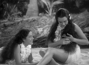 Movie still from “Mutiny on the Bounty” (1935), directed by Frank Lloyd – Two young women sitting on the beach wearing leis; Medium shot, High angle