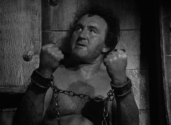 Movie still from “Mutiny on the Bounty” (1935), directed by Frank Lloyd – A man chained to a wooden wall in a room; Medium shot, High angle