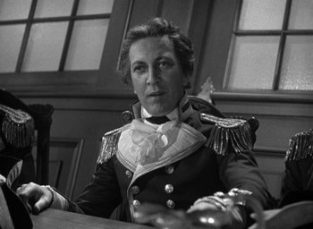 Movie still from “Mutiny on the Bounty” (1935), directed by Frank Lloyd – Black and white photograph of a man in a military uniform sitting at a table; Close Up shot, High angle