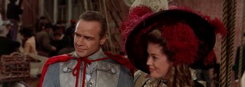 Movie still from “Mutiny on the Bounty” (1962), directed by George Seaton – A man and a woman wearing hats and a dress; Close Up shot, Over the shoulder angle