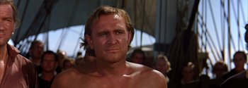 Movie still from “Mutiny on the Bounty” (1962), directed by George Seaton – A shirtless man with long blond hair and no shirt; Close Up shot, Low angle