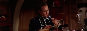Movie still from “Mutiny on the Bounty” (1962), directed by George Seaton – A man in a uniform eating a piece of food; Medium shot, High angle