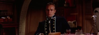Movie still from “Mutiny on the Bounty” (1962), directed by George Seaton – A man in a uniform sitting in front of a table; Close Up shot, Low angle