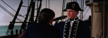 Movie still from “Mutiny on the Bounty” (1962), directed by George Seaton – A man in a uniform talking to another man on a boat; Medium shot, Over the shoulder angle