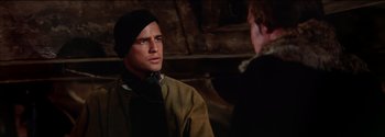 Movie still from “Mutiny on the Bounty” (1962), directed by George Seaton – A man wearing a black hat and a brown jacket; Close Up shot, Over the shoulder angle