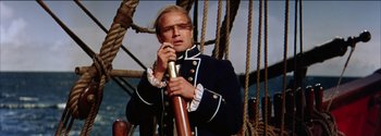 Movie still from “Mutiny on the Bounty” (1962), directed by George Seaton – A man in a sailor's uniform standing on a boat; Medium shot, Low angle