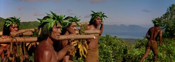 Movie still from “Mutiny on the Bounty” (1962), directed by George Seaton – A group of people in a field with bananas on their heads; Medium shot, Low angle
