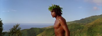 Movie still from “Mutiny on the Bounty” (1962), directed by George Seaton – A man with a flower in his hair standing on top of a hill; Medium shot, Low angle