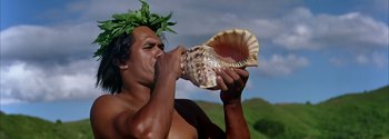 Movie still from “Mutiny on the Bounty” (1962), directed by George Seaton – A man holding a large seashell up to his mouth; Close Up shot, Low angle