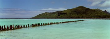 Movie still from “Mutiny on the Bounty” (1962), directed by George Seaton – A body of water that has some rocks in the water; Extreme Wide shot, High angle