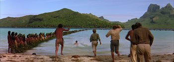 Movie still from “Mutiny on the Bounty” (1962), directed by George Seaton – A group of people standing on top of a sandy beach; Extreme Wide shot, High angle
