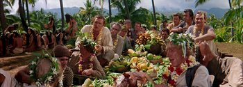 Movie still from “Mutiny on the Bounty” (1962), directed by George Seaton – A group of people sitting around a pile of fruit; Wide shot, High angle