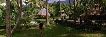 Movie still from “Mutiny on the Bounty” (1962), directed by George Seaton – A woman walking through a lush green field with palm trees and huts; Extreme Wide shot, High angle
