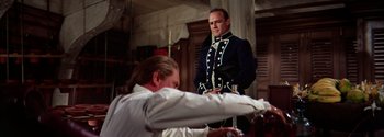 Movie still from “Mutiny on the Bounty” (1962), directed by George Seaton – A man in a suit and tie standing next to another man in a suit and tie; Medium shot, Over the shoulder angle