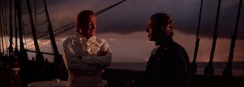 Movie still from “Mutiny on the Bounty” (1962), directed by George Seaton – Two men are standing next to each other in front of a body of water; Medium shot, Over the shoulder angle