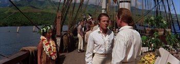 Movie still from “Mutiny on the Bounty” (1962), directed by George Seaton – A man in a white shirt standing next to another man in a white shirt; Medium shot, Over the shoulder angle