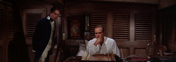 Movie still from “Mutiny on the Bounty” (1962), directed by George Seaton – A man sitting in front of a chess board in a room; Medium shot, High angle