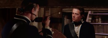 Movie still from “Mutiny on the Bounty” (1962), directed by George Seaton – A man in a suit and tie is talking to another man in a suit and tie; Medium shot, Over the shoulder angle