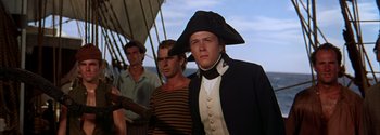Movie still from “Mutiny on the Bounty” (1962), directed by George Seaton – A man in a pirate's hat stands on a boat; Medium shot, Low angle