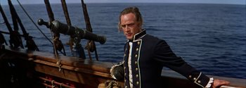 Movie still from “Mutiny on the Bounty” (1962), directed by George Seaton – A man standing on top of a boat near the ocean; Medium shot, Over the shoulder angle
