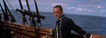 Movie still from “Mutiny on the Bounty” (1962), directed by George Seaton – A man standing on top of a boat near the ocean; Medium shot, Over the shoulder angle