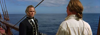 Movie still from “Mutiny on the Bounty” (1962), directed by George Seaton – Two men on a boat in front of a body of water; Medium shot, Over the shoulder angle