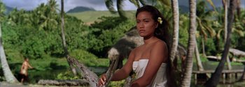 Movie still from “Mutiny on the Bounty” (1962), directed by George Seaton – A beautiful young woman holding a branch while standing next to a tree; Medium shot, Over the shoulder angle