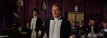 Movie still from “Mutiny on the Bounty” (1962), directed by George Seaton – A man in a suit standing in front of other men; Medium shot, Over the shoulder angle
