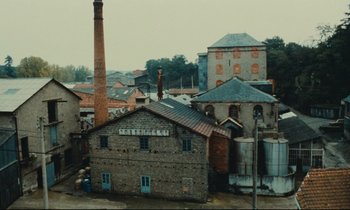 Movie still from “My American Uncle” (1980), directed by Alain Resnais – An old brick building with a brick chimney in front of it; Extreme Wide shot, High angle