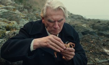 Movie still from “My American Uncle” (1980), directed by Alain Resnais – An older man holding a crab in his hands; Close Up shot, High angle