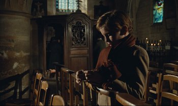 Movie still from “My American Uncle” (1980), directed by Alain Resnais – A young boy sitting in a pew in a church; Medium shot, Low angle