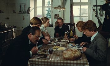Movie still from “My American Uncle” (1980), directed by Alain Resnais – A group of people sitting around a table eating food; Wide shot, High angle