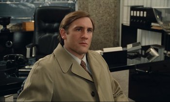 Movie still from “My American Uncle” (1980), directed by Alain Resnais – A man in a suit and tie sitting in an office chair; Medium shot, Low angle