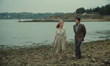Movie still from “My American Uncle” (1980), directed by Alain Resnais – A man and a woman walking on the shore of a body of water; Wide shot, Low angle