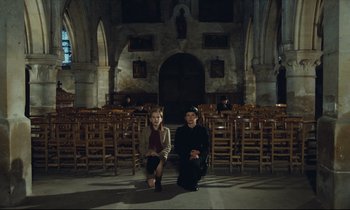 Movie still from “My American Uncle” (1980), directed by Alain Resnais – A man and a woman kneeling in front of an altar; Wide shot, High angle