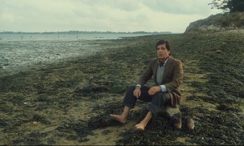Movie still from “My American Uncle” (1980), directed by Alain Resnais – A man sitting on the ground on the beach; Wide shot, High angle