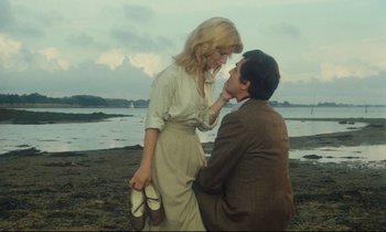 Movie still from “My American Uncle” (1980), directed by Alain Resnais – A man kneeling down next to a woman on the beach; Medium shot, High angle