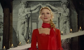 Movie still from “My American Uncle” (1980), directed by Alain Resnais – A woman in a red dress standing in front of statues; Medium shot, Low angle
