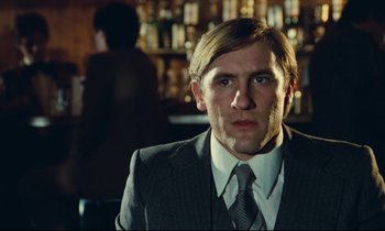 Movie still from “My American Uncle” (1980), directed by Alain Resnais – A man wearing a suit and tie in a bar; Close Up shot, Over the shoulder angle