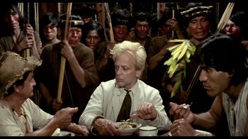 Movie still from “My Best Fiend” (1999), directed by Werner Herzog – A man sitting at a table with a bowl of food surrounded by people; Medium shot, Over the shoulder angle