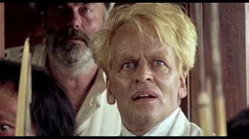 Movie still from “My Best Fiend” (1999), directed by Werner Herzog – A man with blonde hair and blue eyes stares at the camera; Close Up shot, Low angle